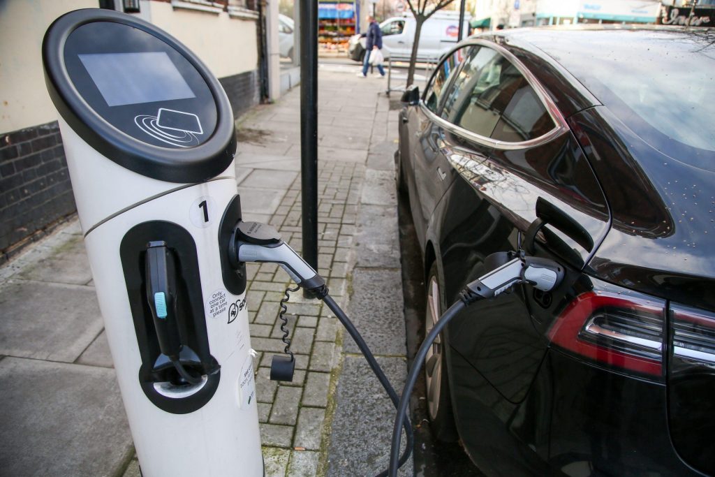 Black electric car charging on the side of the road using an electric car charging point